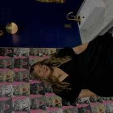 Standing in front of a pink printed wall and smiling.