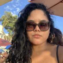 Woman with a brown hair, sun glasses and golden earrings at the beach. 