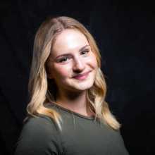 I appear smiling against a black backdrop wearing a green shirt. I am white with blonde hair and blue eyes.