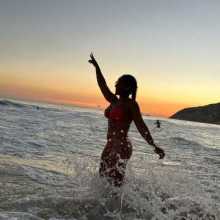 A woman stands on the beach at sunset.