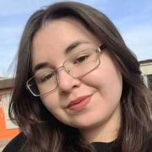 A picture of me smiling for the camera (like always). A bit longer than shoulders-lenght dark blonde hair, brown eyes, rectangular glasses, round face.