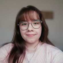 Picture of a brunette woman with glasses and a light pink sweater 