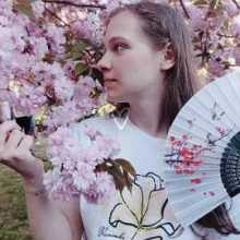 a girl with a fan in her hand near a cherry blossom