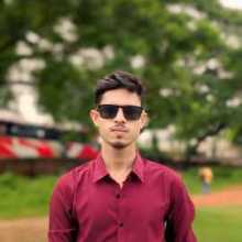 ​"A young man wearing a red shirt and black sunglasses, standing outdoors."
