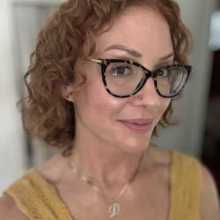 Woman with medium length curly copper hair, glasses, fair skin.