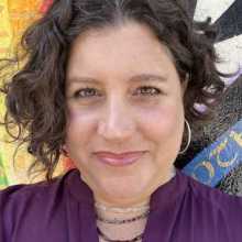 Smiling woman, purple shirt, medium length curly brown hair