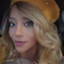 Headshot of a light skinned, african american woman with long blonde hair wearing a tan hat.