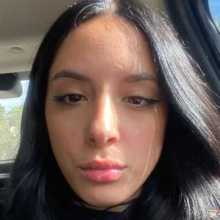 Close-up selfie inside a car, sunlight on her face, long dark hair, and winged eyeliner.