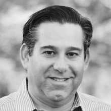 Headshot of a smiling person with short brown hair, wearing a blue shirt, against a neutral background