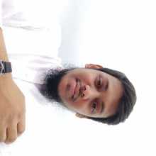A young man wearing a white outfit and a wristwatch taking a selfie.