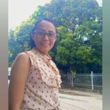 Brazilian woman smiling outdoors, wearing glasses, with trees in the background.