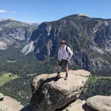 Man standing on top of rock at the top of a cliff.