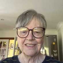An older woman with glasses smiling.