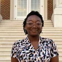 Picture of a young African-American woman. She is wearing glasses and a multicolored top. 