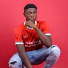 An image of me in a pose for the camera. Am wearing a Liverpool jersey and a light blue jean.
