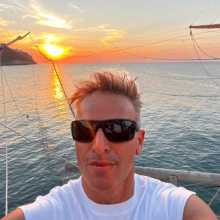 A selfie about me wearing sunglasses on a wooden trabucco in Puglia with a stunning sunset over the sea.