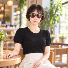A woman wearing sunglasses and a black top, sitting at an outdoor café.